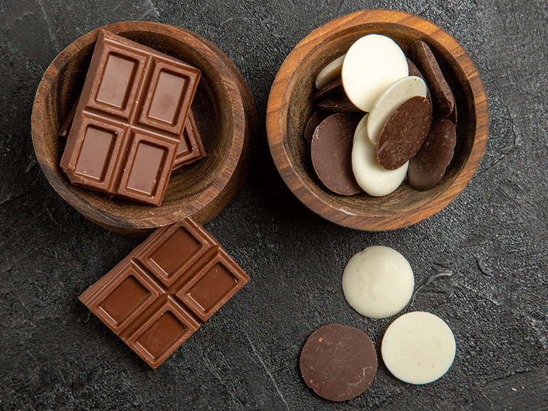 Assorted dark chocolate bar and white chocolate wafers on a slate board