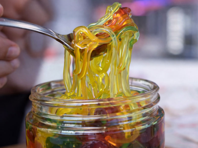 Primer plano de una cuchara sacando gomitas pegajosas empapadas en almíbar de un frasco de gomitas líquidas.